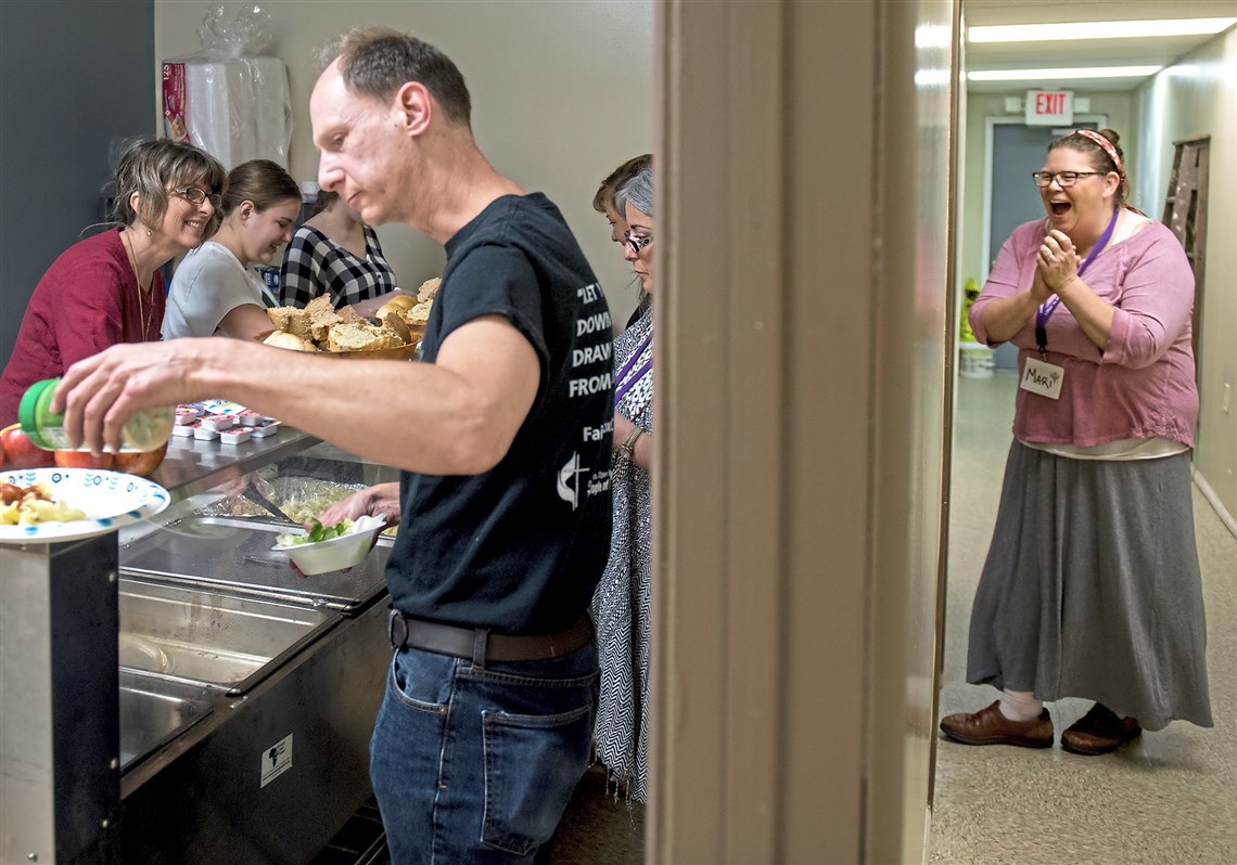 Mari Rolewicz, far right, of Sharpsburg, laughs while waiting in line for her food during a community dinner with the Circles program through Roots of Faith on May 1 at the Roots of Faith community storefront church in Sharpsburg.